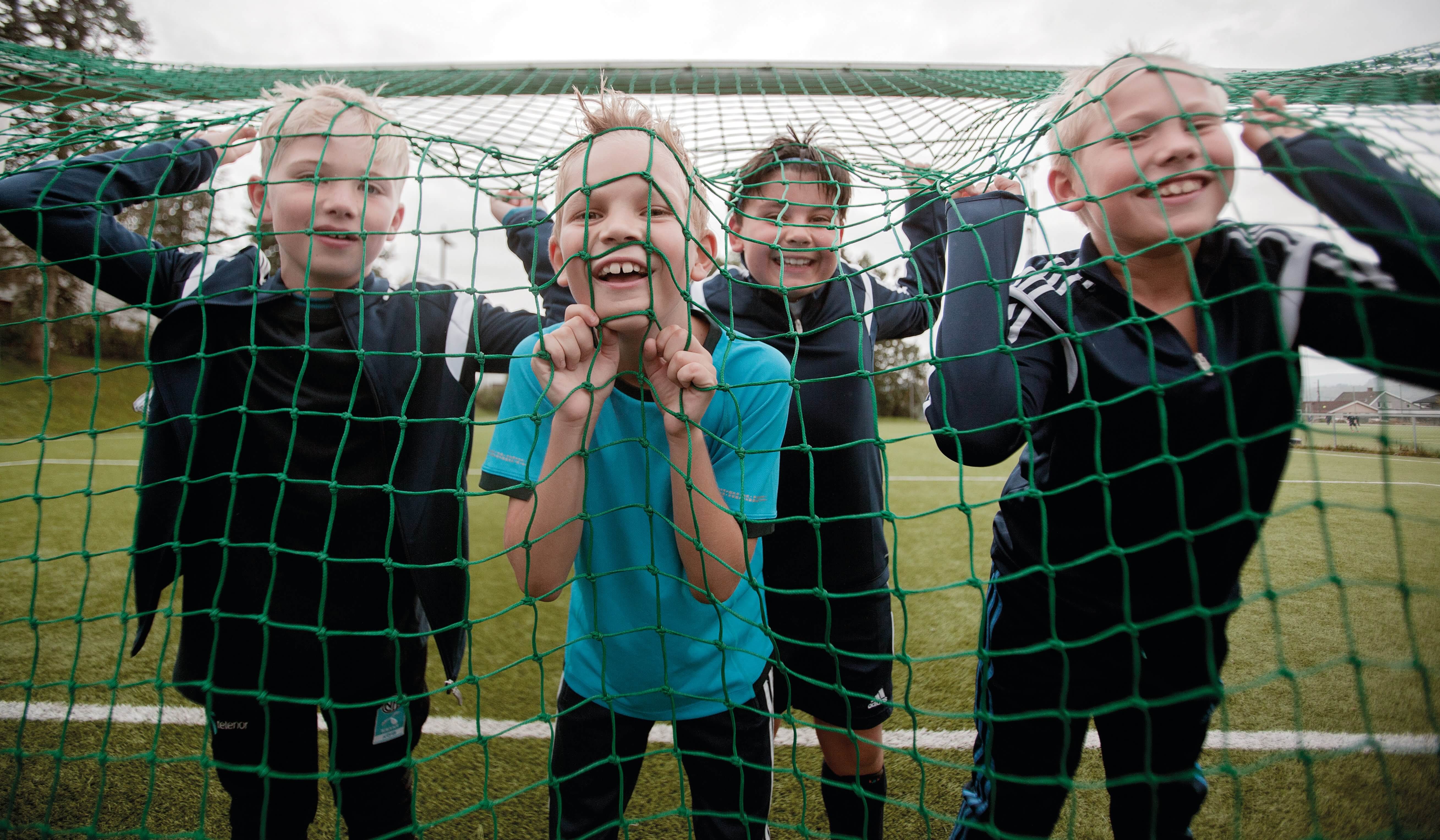 Fire gutter står inne i et fotballmål og smiler.