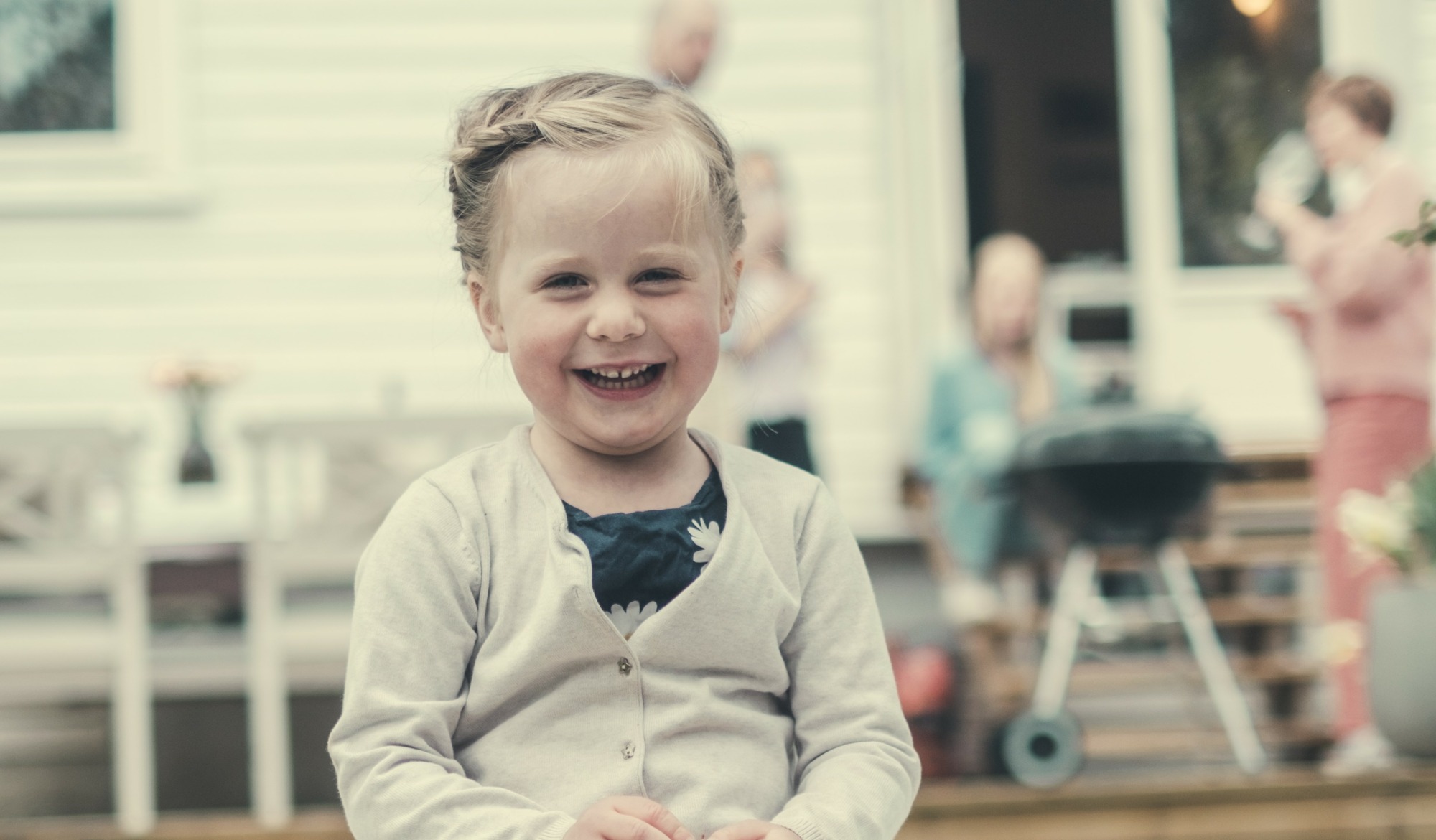 Foto av jente som smiler mot kamera. Folk i bakgrunnen som hygger seg på en sommerdag.