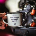 Bilde av en kaffekopp med påskriften ekte kapteiner drikker kaffe. Man kan skimte en båtmotor i bakgrunnen.