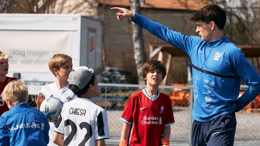 Trener organiserer barn på en fotballbane. Han peker ut av bildet og barna ser