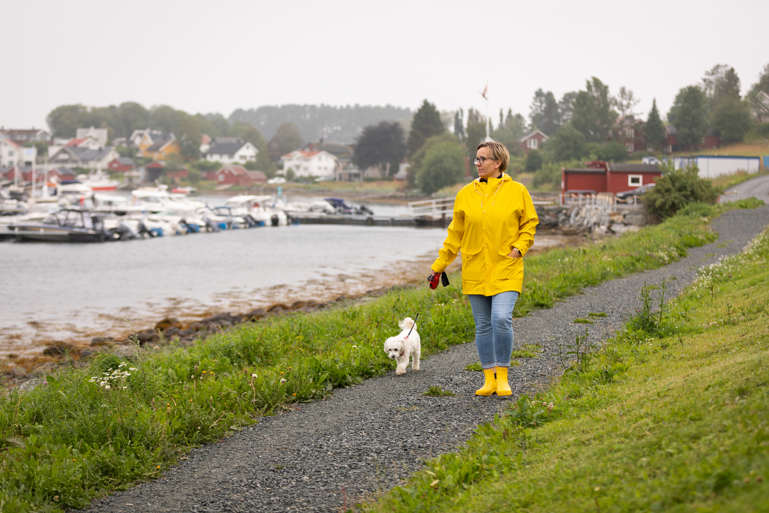 Maria som går en tur med hunden. Hun går tur med gul regnjakke og gule gummisko.