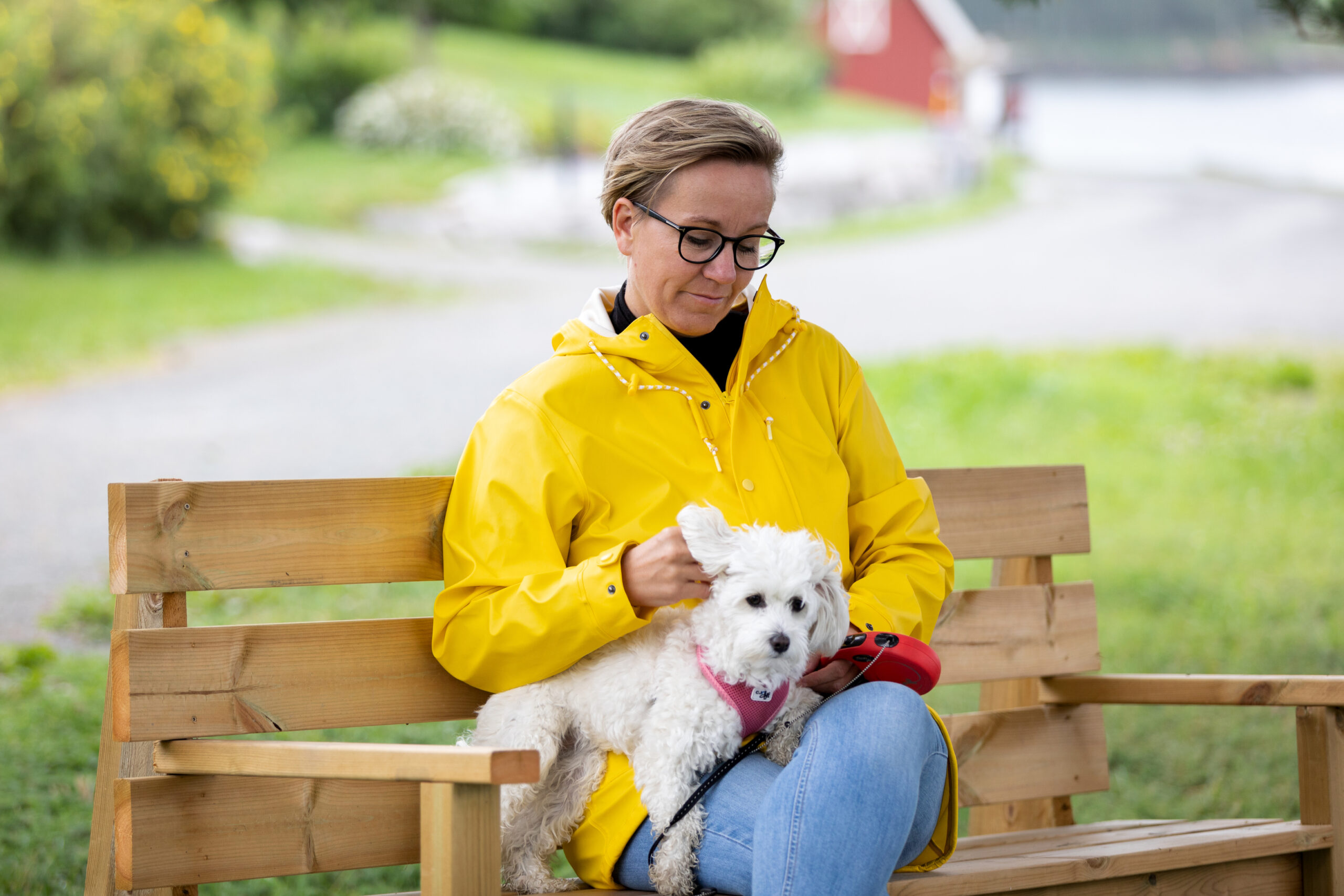 Bilde av Maria som holder en hund. Hun sitter på en benk i en gul regnjakke.