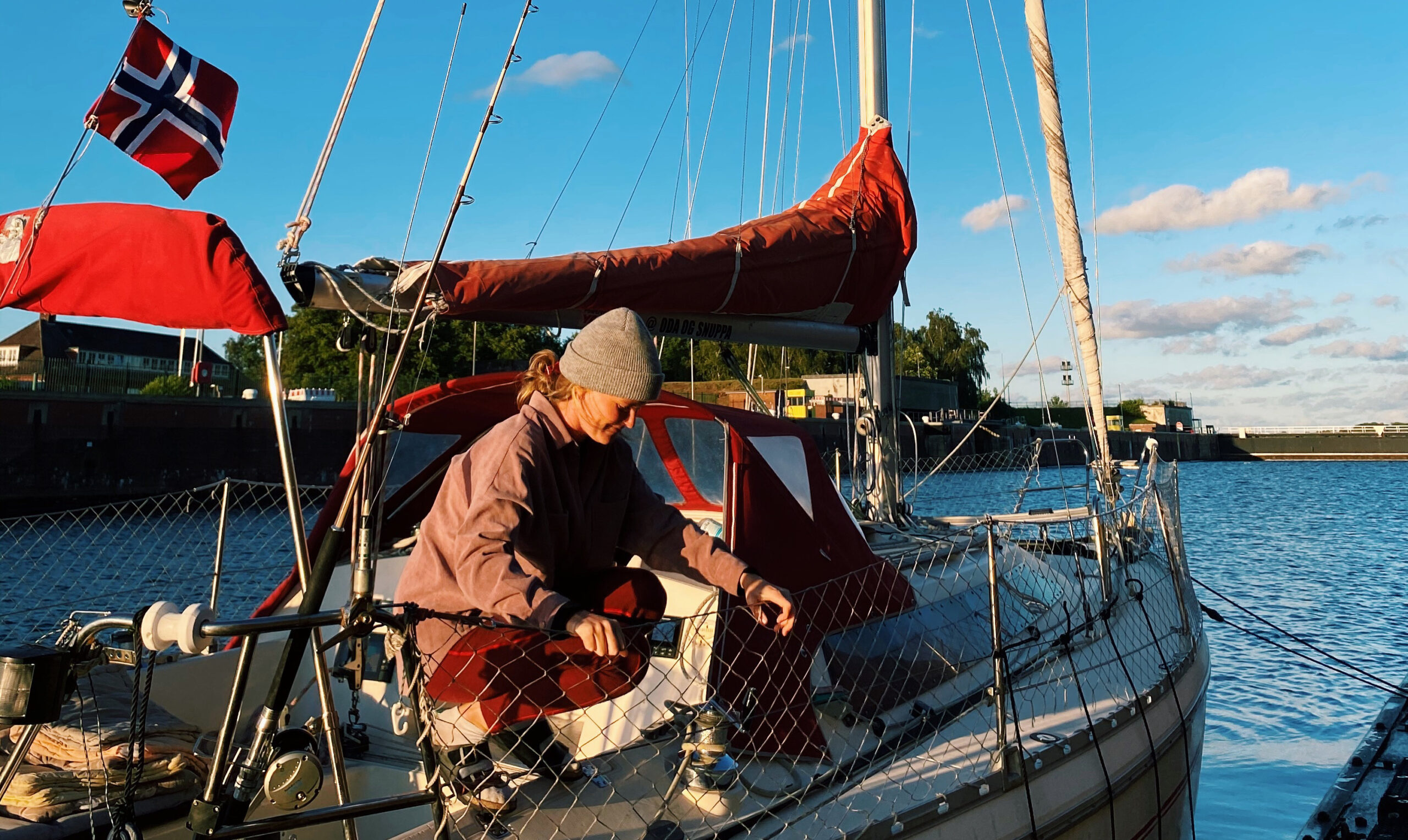 Oda på seilbåten på langsiden. Hun fisker noe på båten og det er blå himmel og sol.