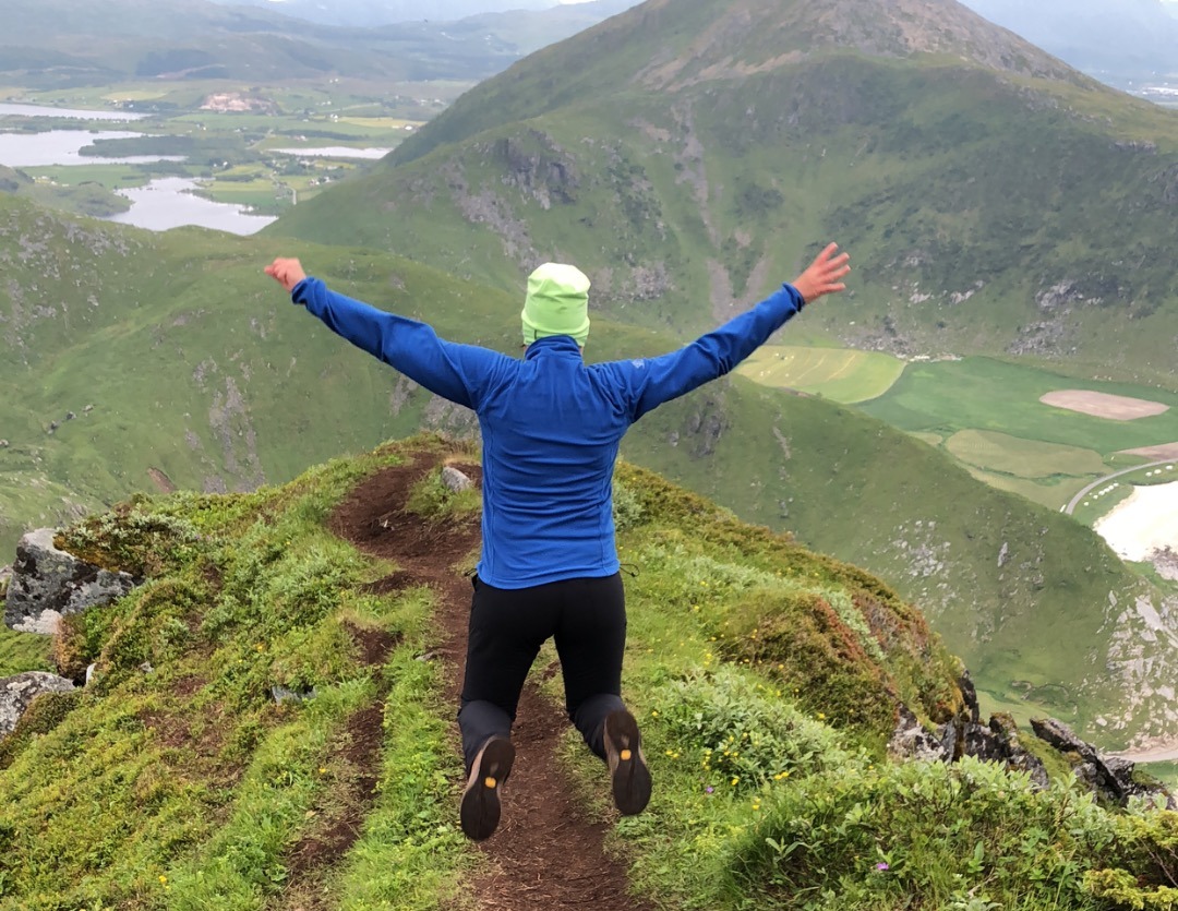 Wenche hopper på toppet av et fjell. Hun er ute i norsk natur og har på seg en blå fleece genser.