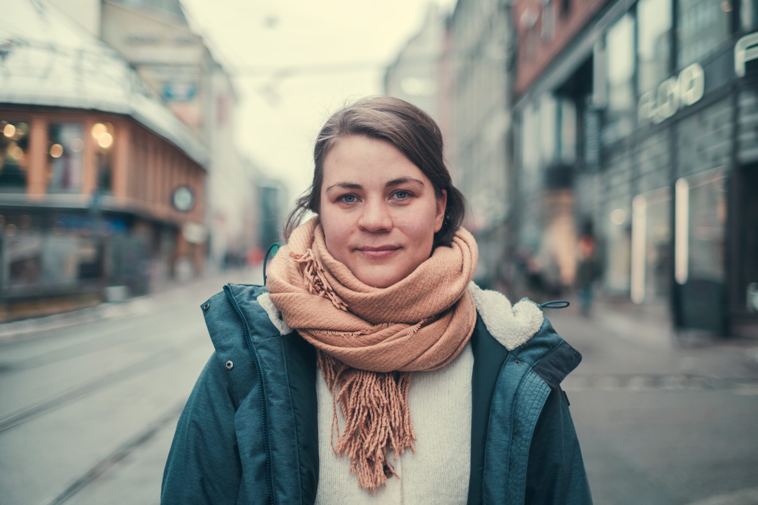 Ragnhild som står i gaten i Oslo med skjerf rundt halsen. Hun smiler forsiktig til kamera.