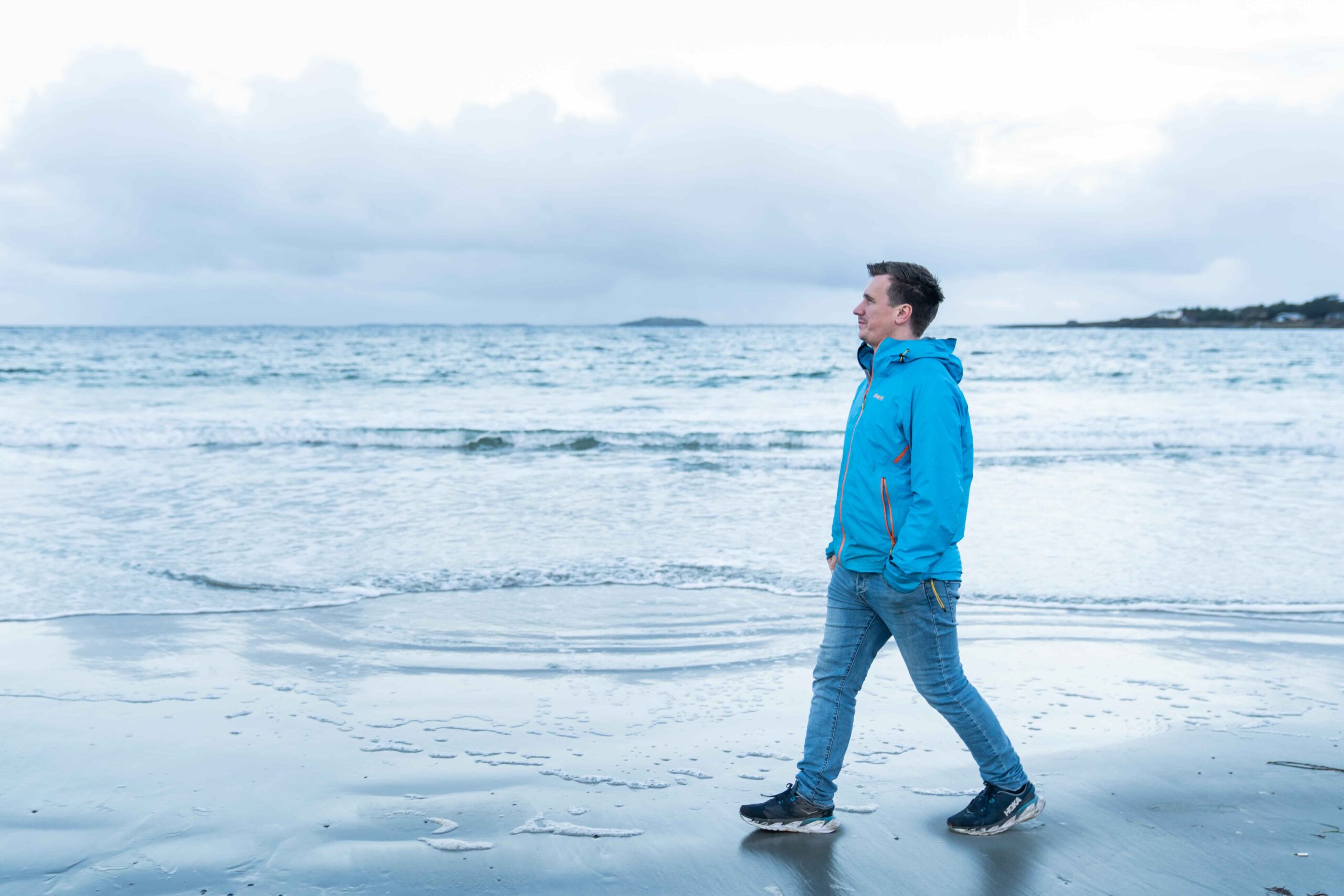 Michal som går på en strand, han har på seg en blå jakke. 