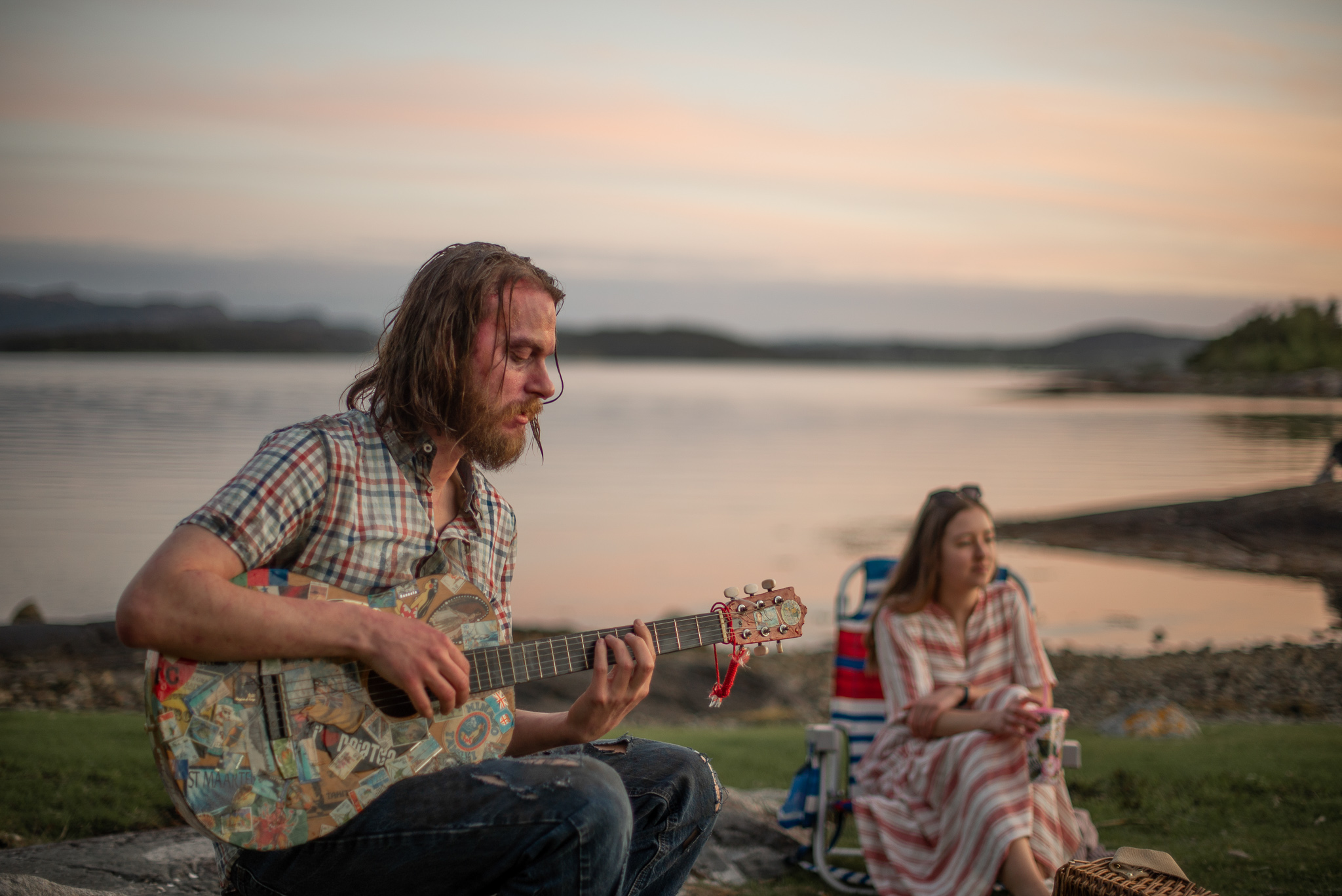 Bilde av en sen sommerdag en mann som holder en gitar og synger og en dame i bakgrunnen med et teppe rundt seg.