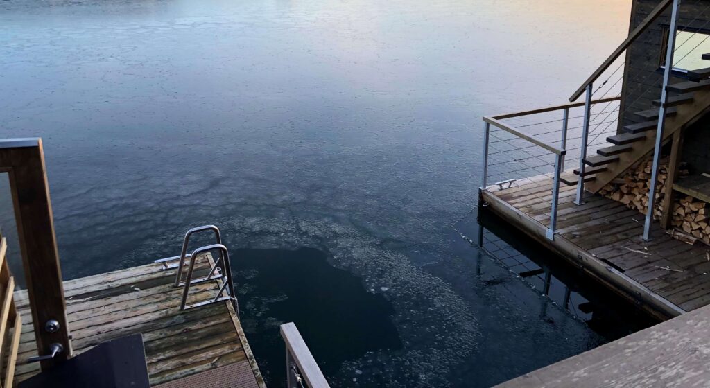 Brygge med badestige som går ned i vann med tynt islag. Foto.