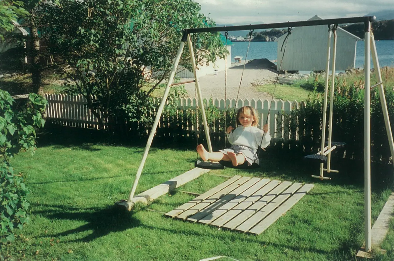 Et gammel bilde av en liten jente som husker i en hage med sjøen i bakgrunnen.