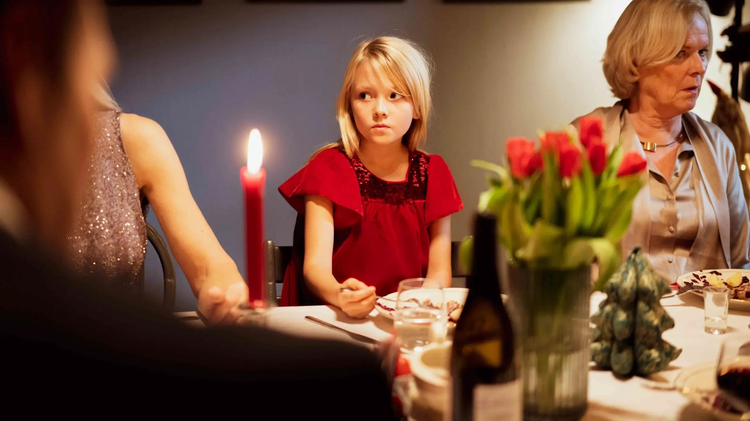 Jente sitter rundt bordet på en julemiddag og ser litt skeptisk ut. Det er blide voksne rundt henne.