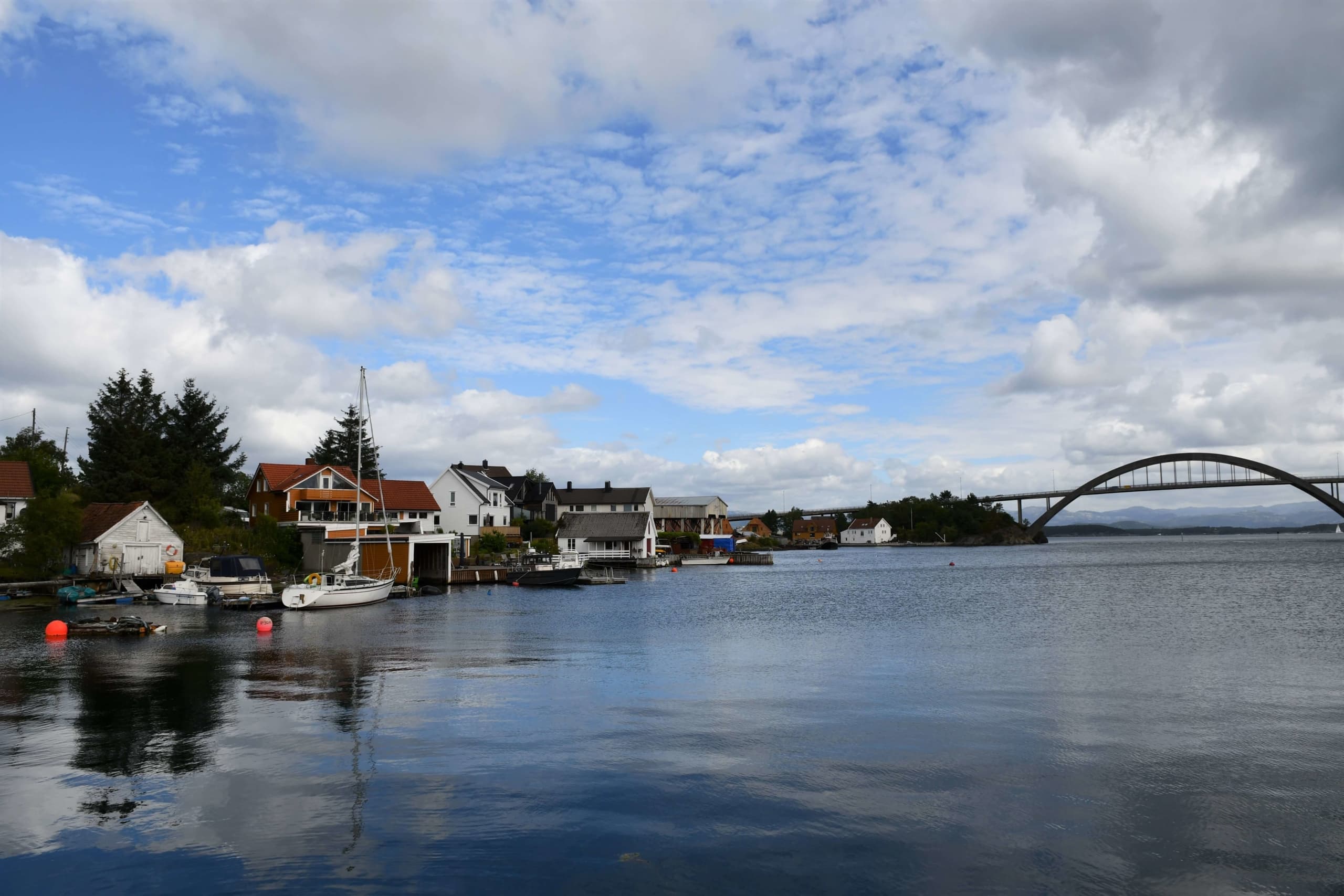 Kystlandskap med hytter, hus, speilblank sjø - og en bro i bakgrunnen