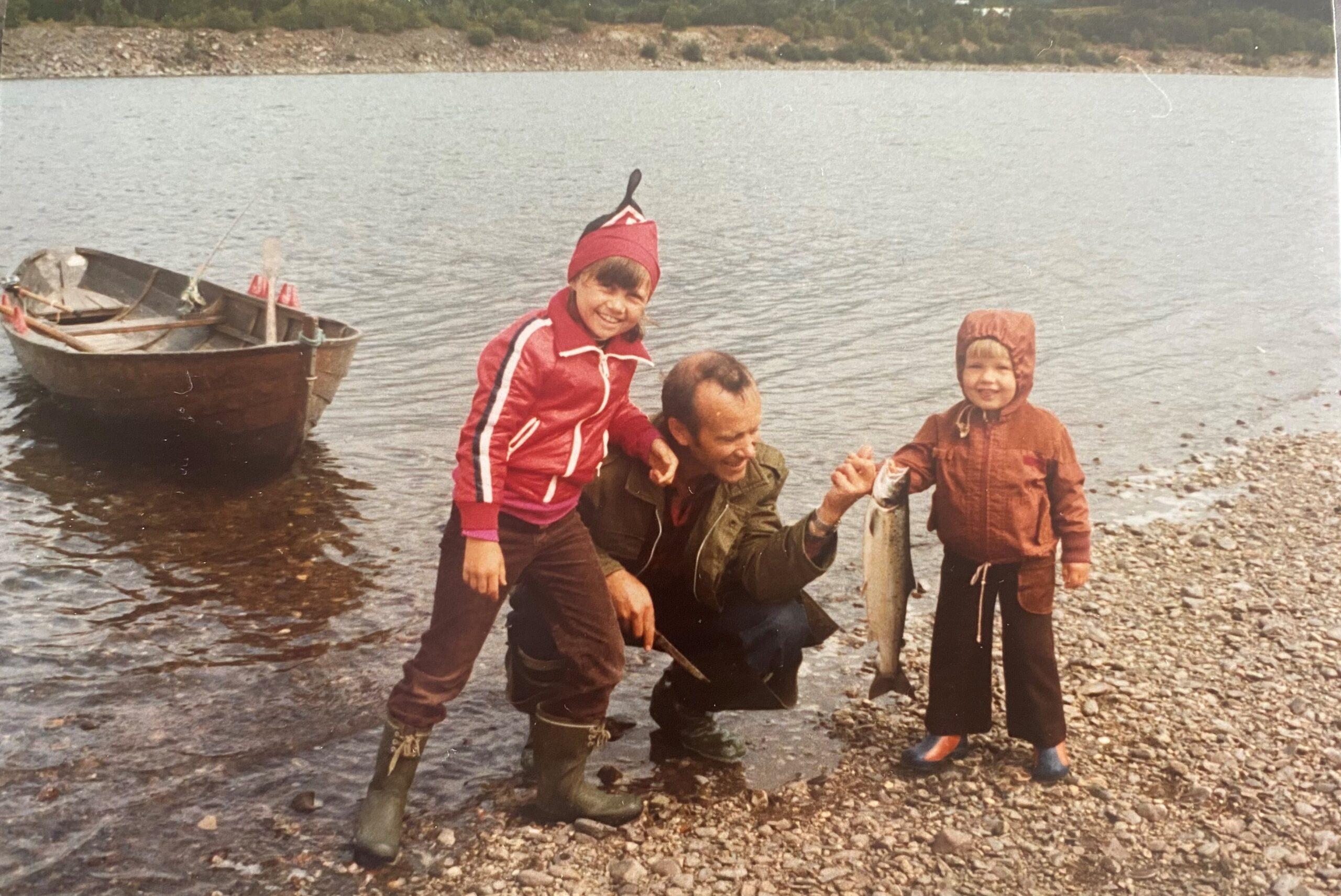 Barnebilde av at famlien fisker, de holder en fisk og det er en robåt i bakgrunnen.