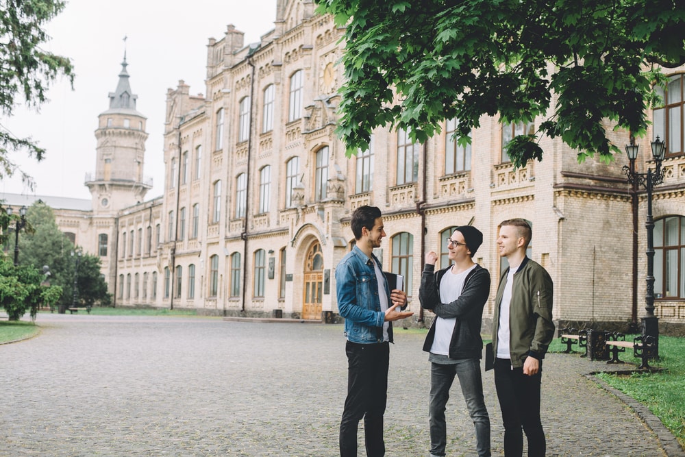 3 menn som står utenfor en skole og snakker sammen. 