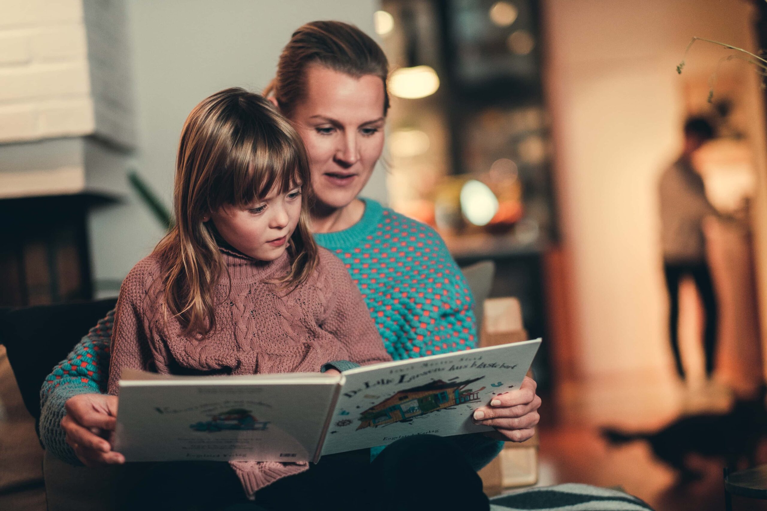 Et barn som sitter på fanget til en dame, de leser en bok.