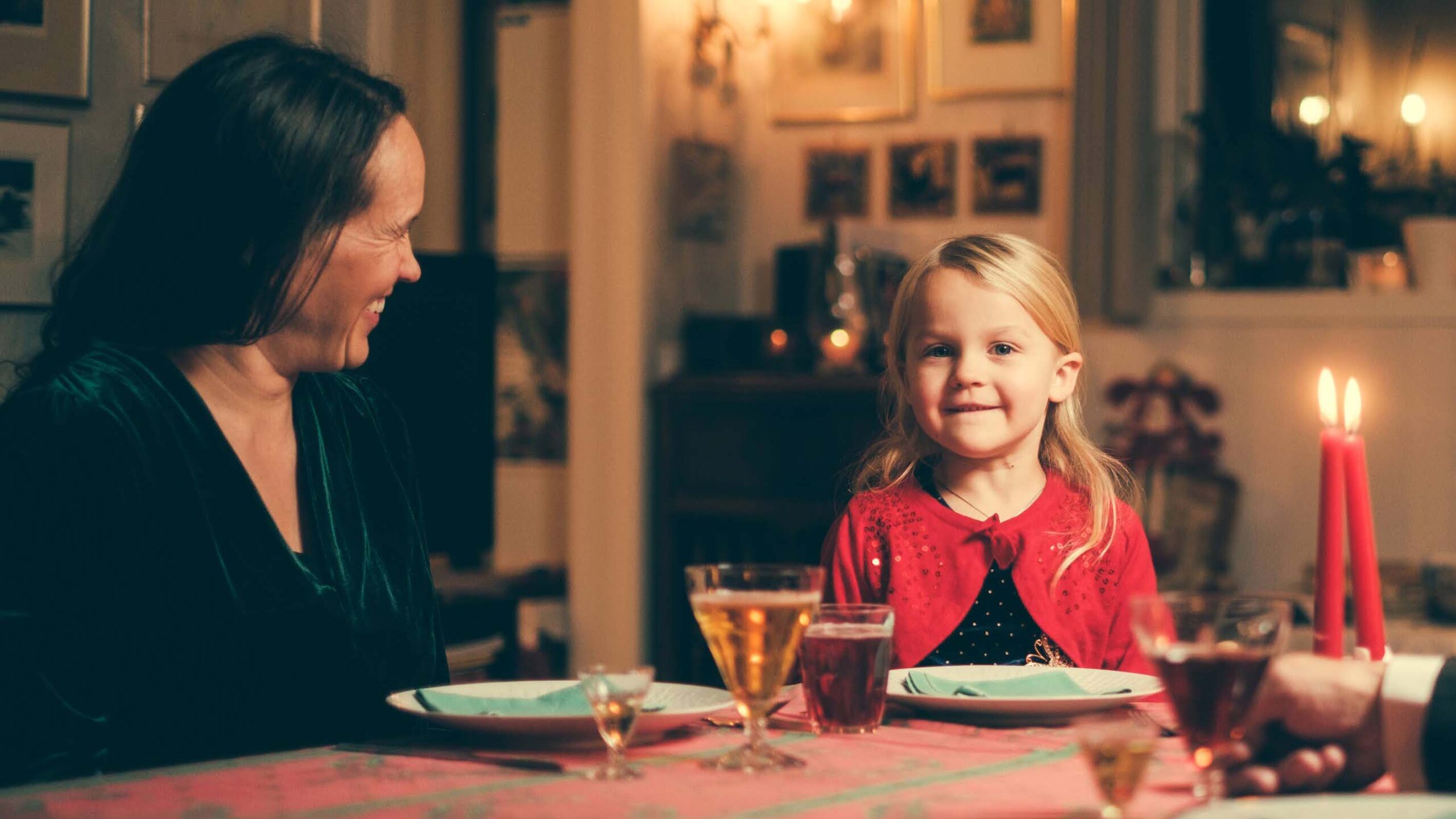 Bilde av jente som sitter ved et bord sammen med voksen dame. Bordet er dekket og det er drikke i glassene.