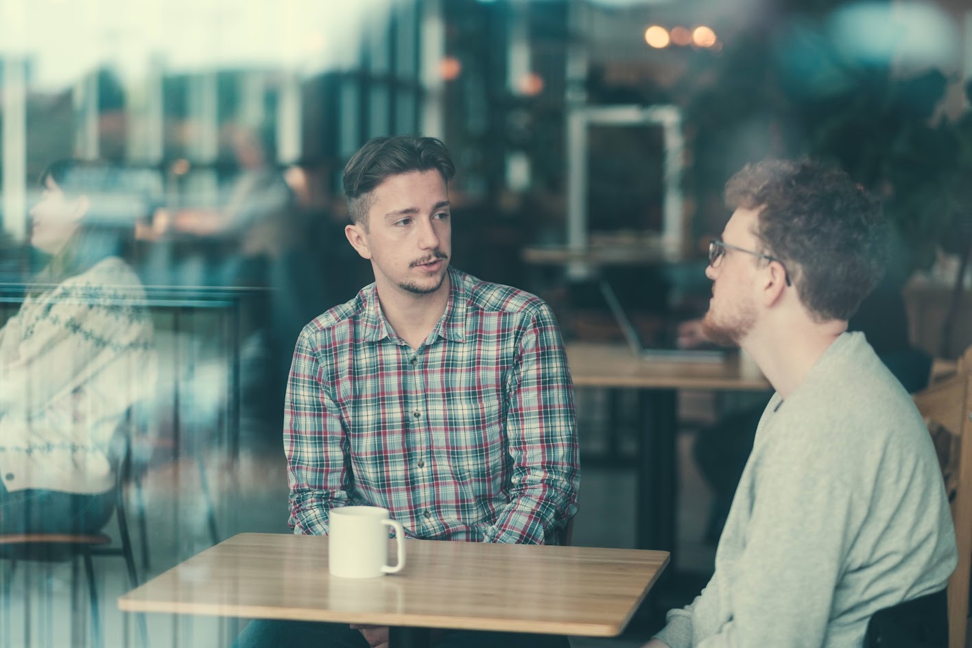 To unge menn sitter på kafé og snakker sammen over en kopp kaffe.