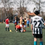 Gutt står alene på banen med ballen i hånde og ser på en mindre gjeng med barn