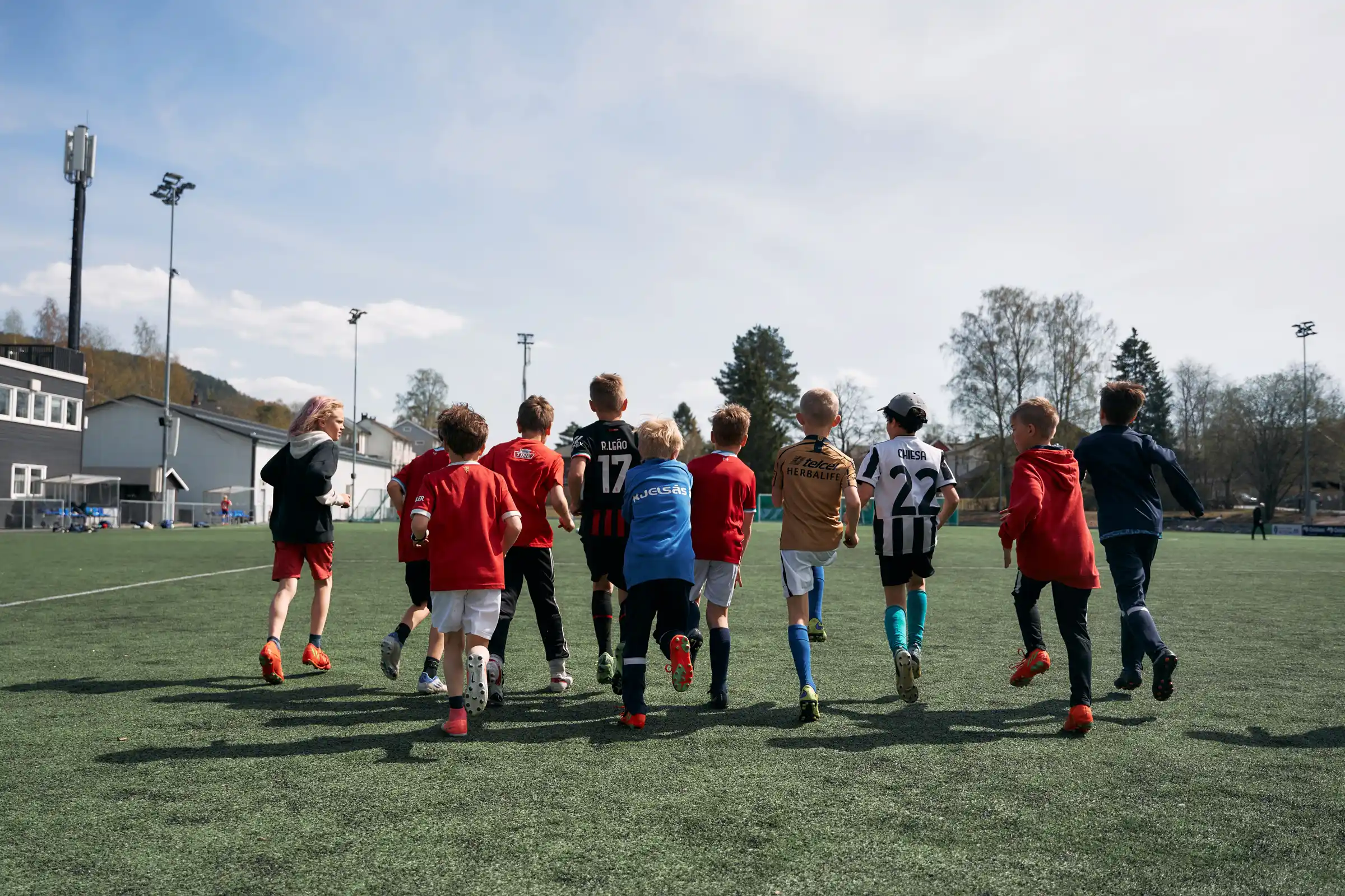 en gjeng med barn på fotballbanen løper vekk fra kamera. De varmer opp på trening.