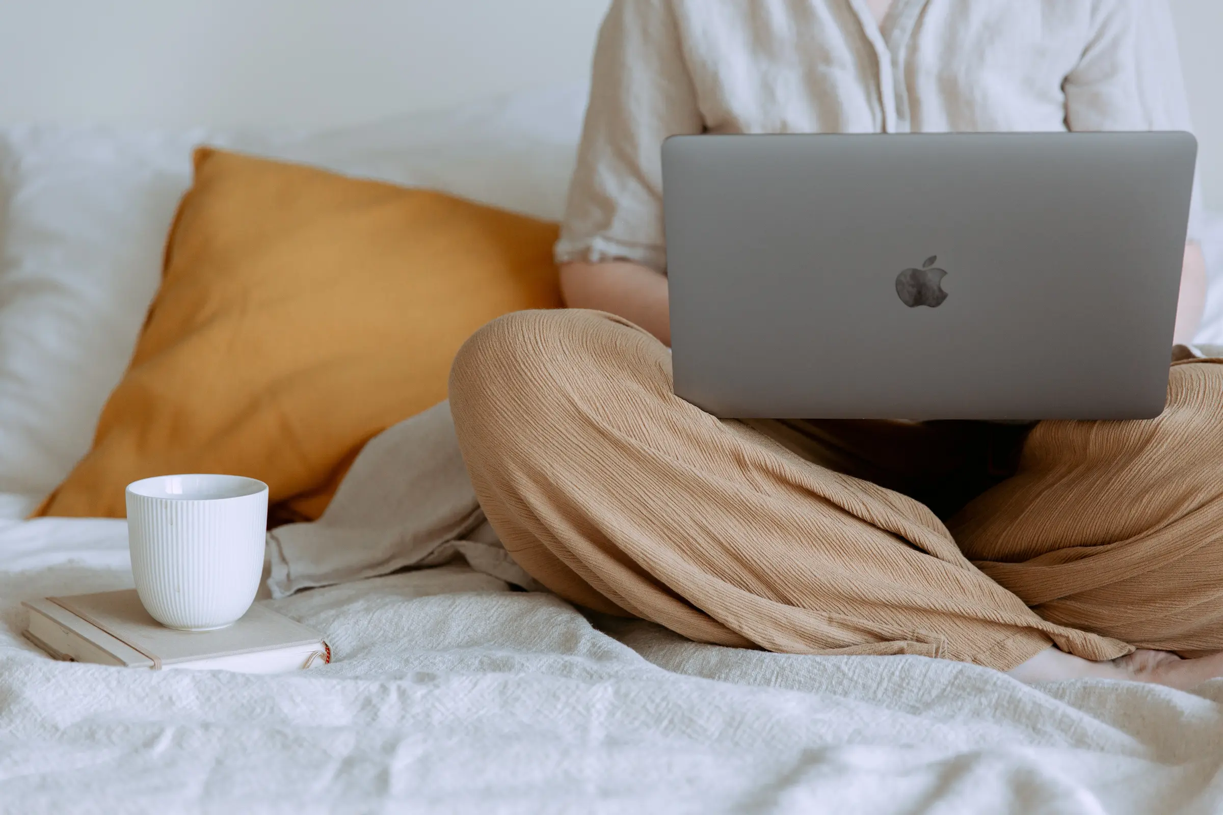 En som sitter med pcen på fanget og en kaffekopp på siden av. Man ser ikke ansiktet til personen.