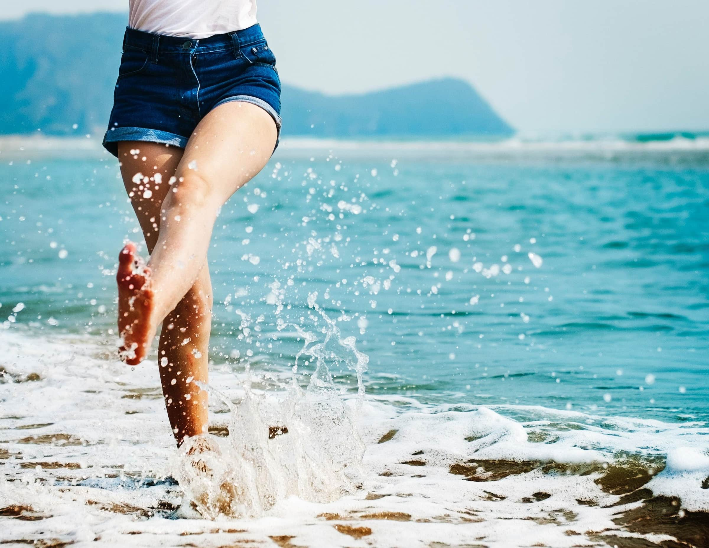 Et bilde av beina til en person som vasser i strandkanten