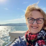Kari henriksten står foran en sjø og tar selfie med blå himmel
