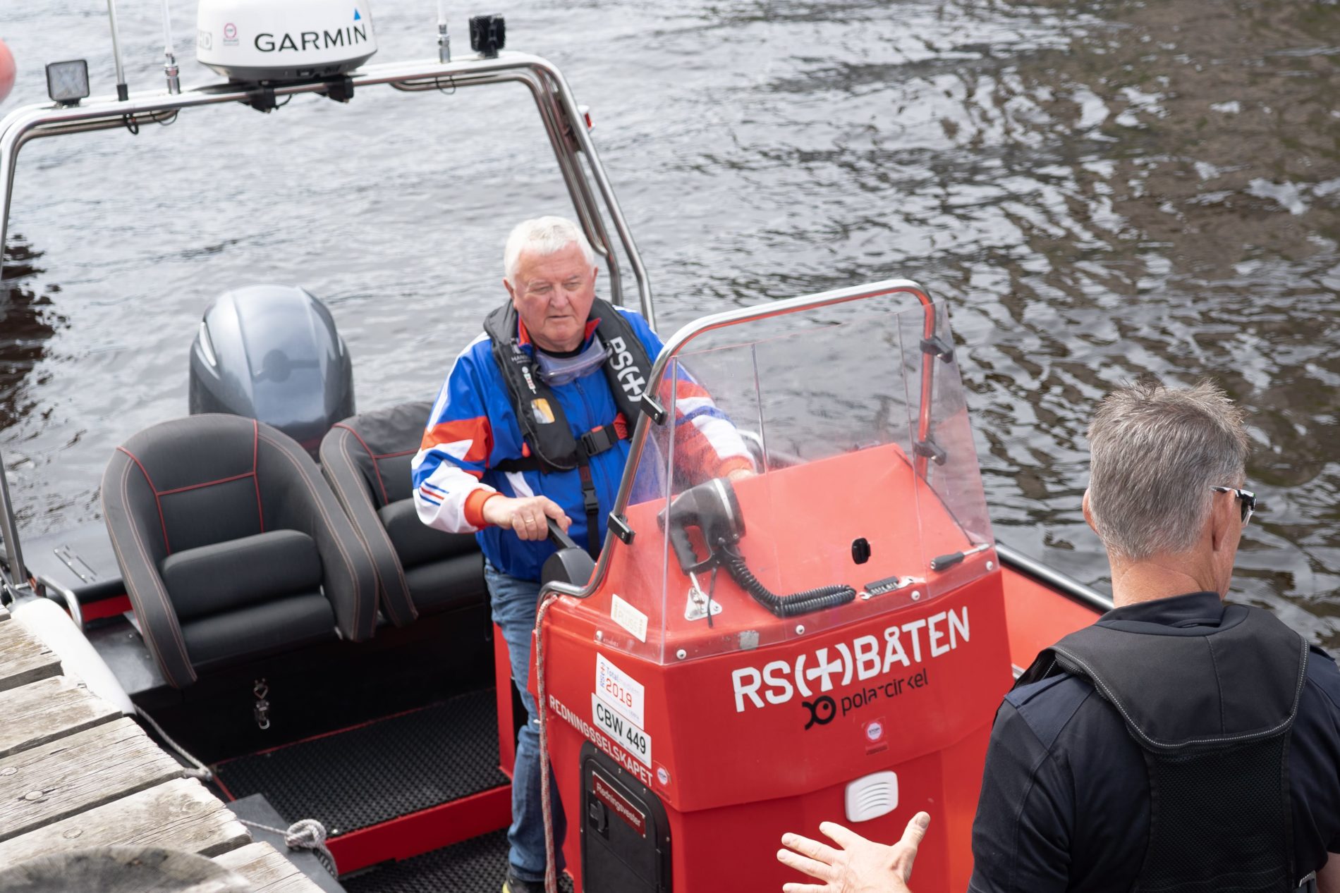 Roar, en godt voksen mann, ikledd blå jakke og redningsvest kjører en båt.