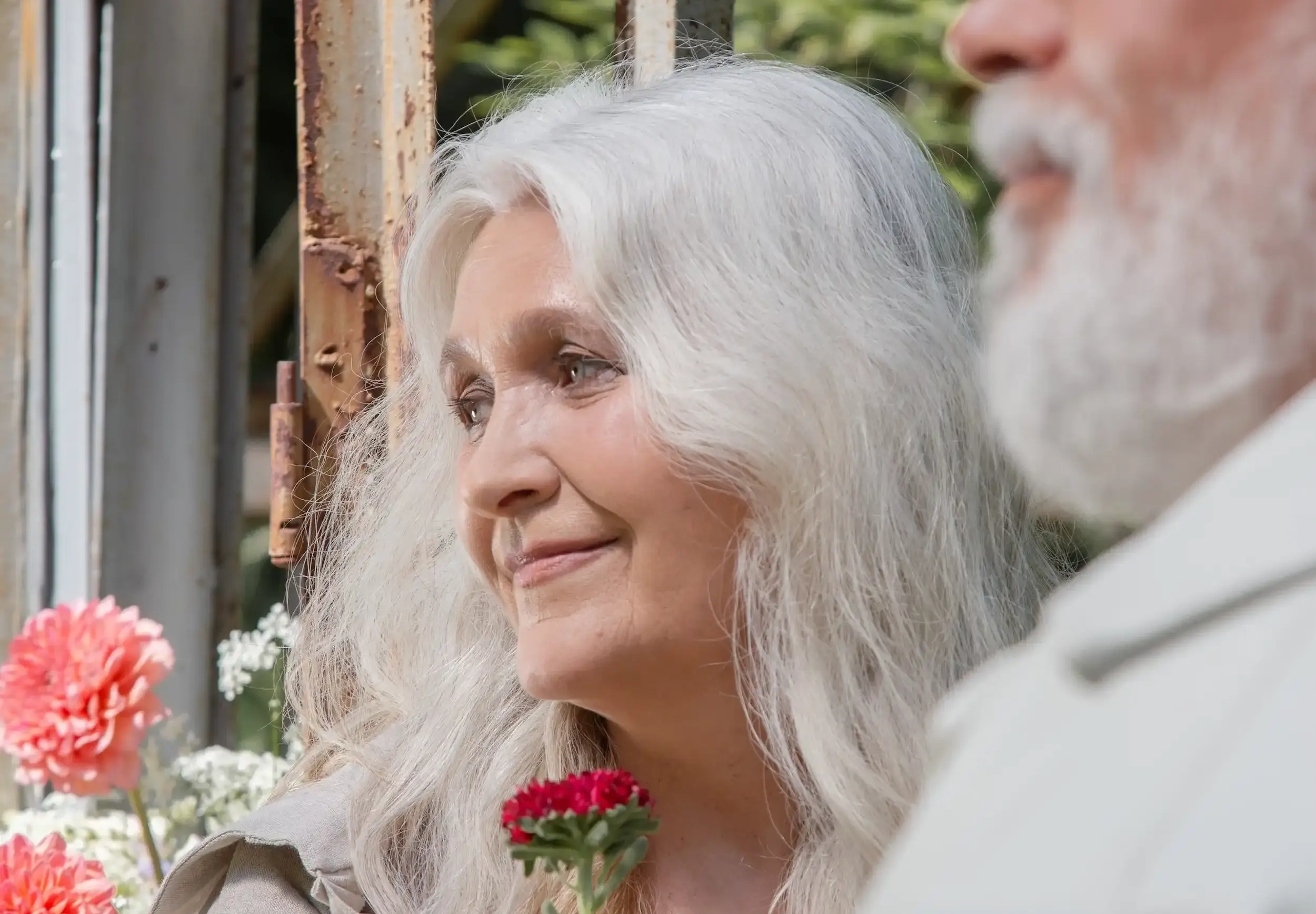 Eldre dame med hvit hår holder en rose, mann med hvitt skjegg i forgrunnen.