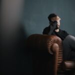 Bilde av en sliten ung mann med alkoholabstinenser som sitter med hodet i hånden i en brun skinnsofa