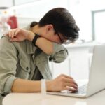 Mann som nyser av en allergisk reaksjon foran sin pc