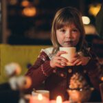 Julepyntet jente sitter med en kopp kakao og ser inn i kamera.