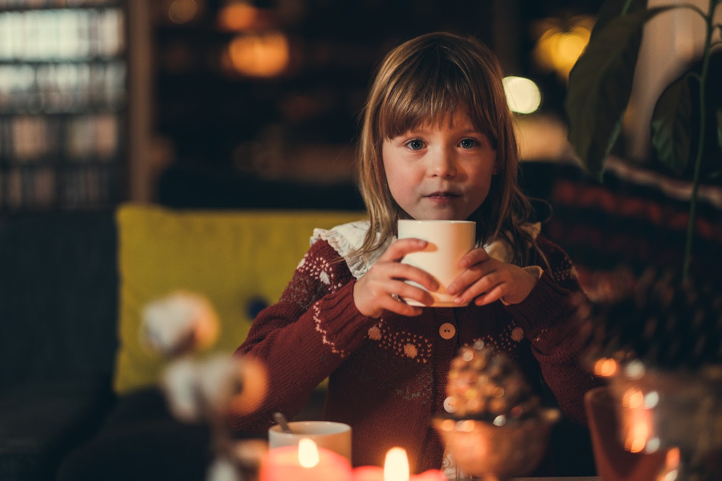 Julepyntet jente sitter med en kopp kakao og ser inn i kamera.