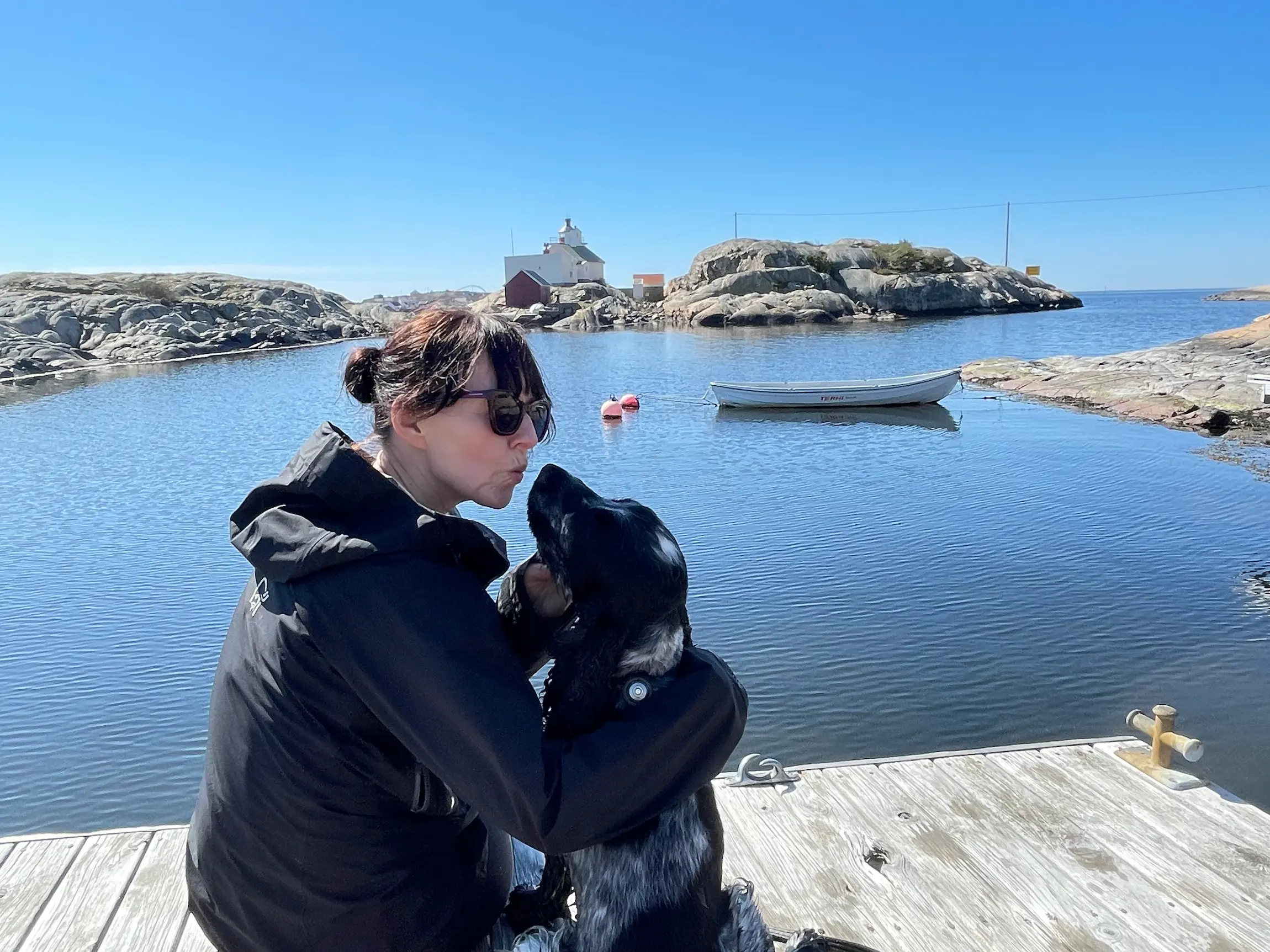 Sitter på en brygge i en skjærgård og koser med en hund. vannet er blikkstille.