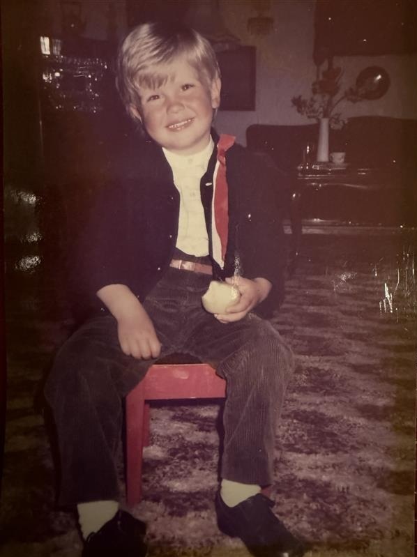 Barnebilde av Ole Erevik. Han har på seg penklær og en rød sløyfe og spiser på et eple.