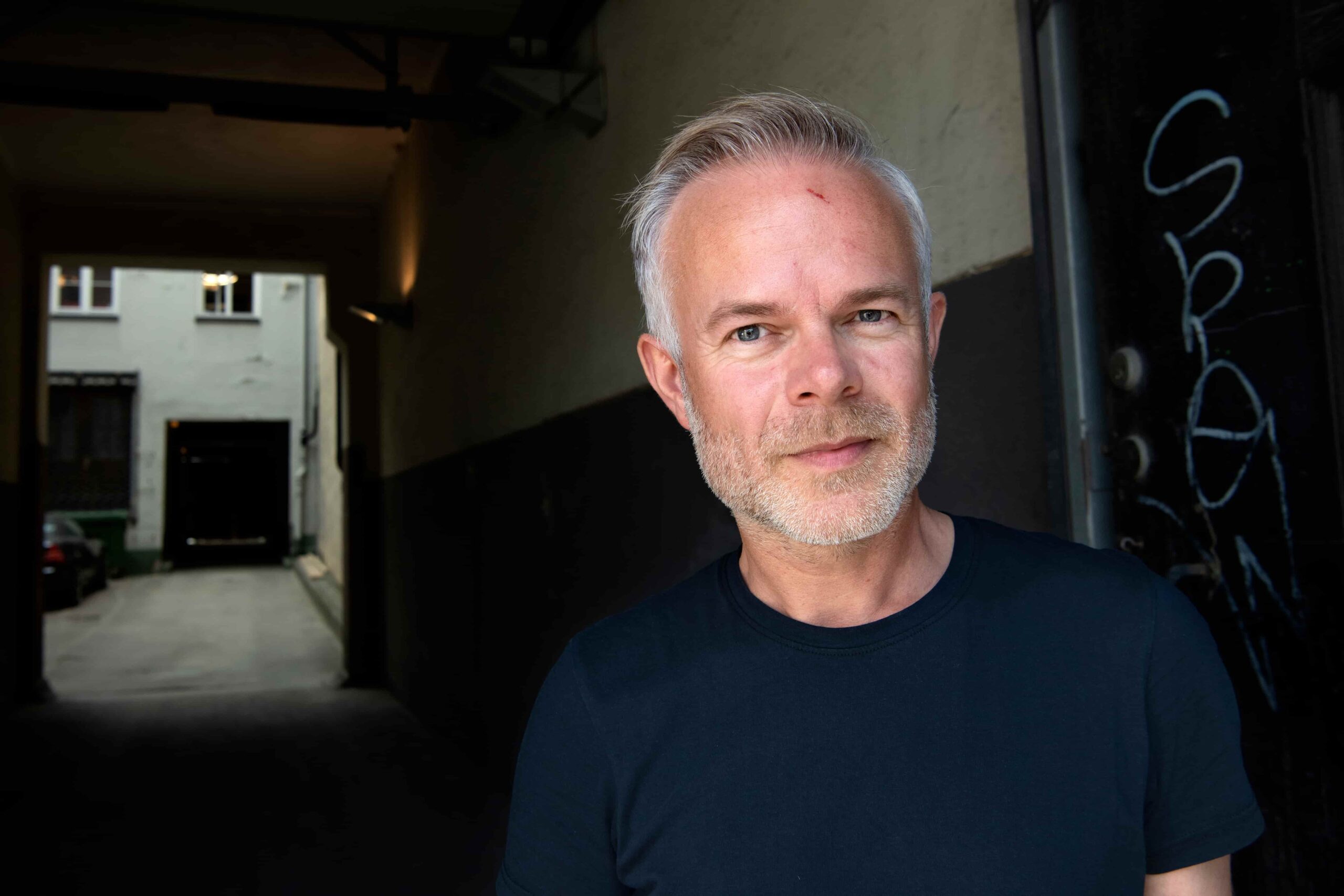 BIlde av Tore Renberg stående i inngangen til et boligbygg i en mørk t-skjorte.