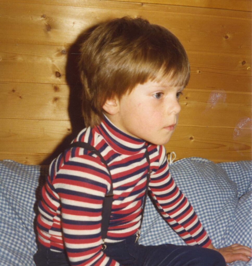 Tore Renberg som barn sitter på sengen i en stripede, langermet trøje og ser foran seg. 