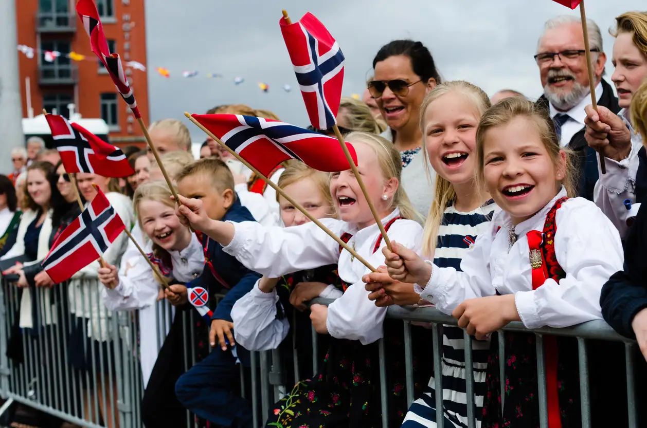Festkledde barn og voksne med norske flagg står og venter på 17. mai-toget.