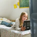 Jente på omtrent 12 år ligger på senga og leser en bok.