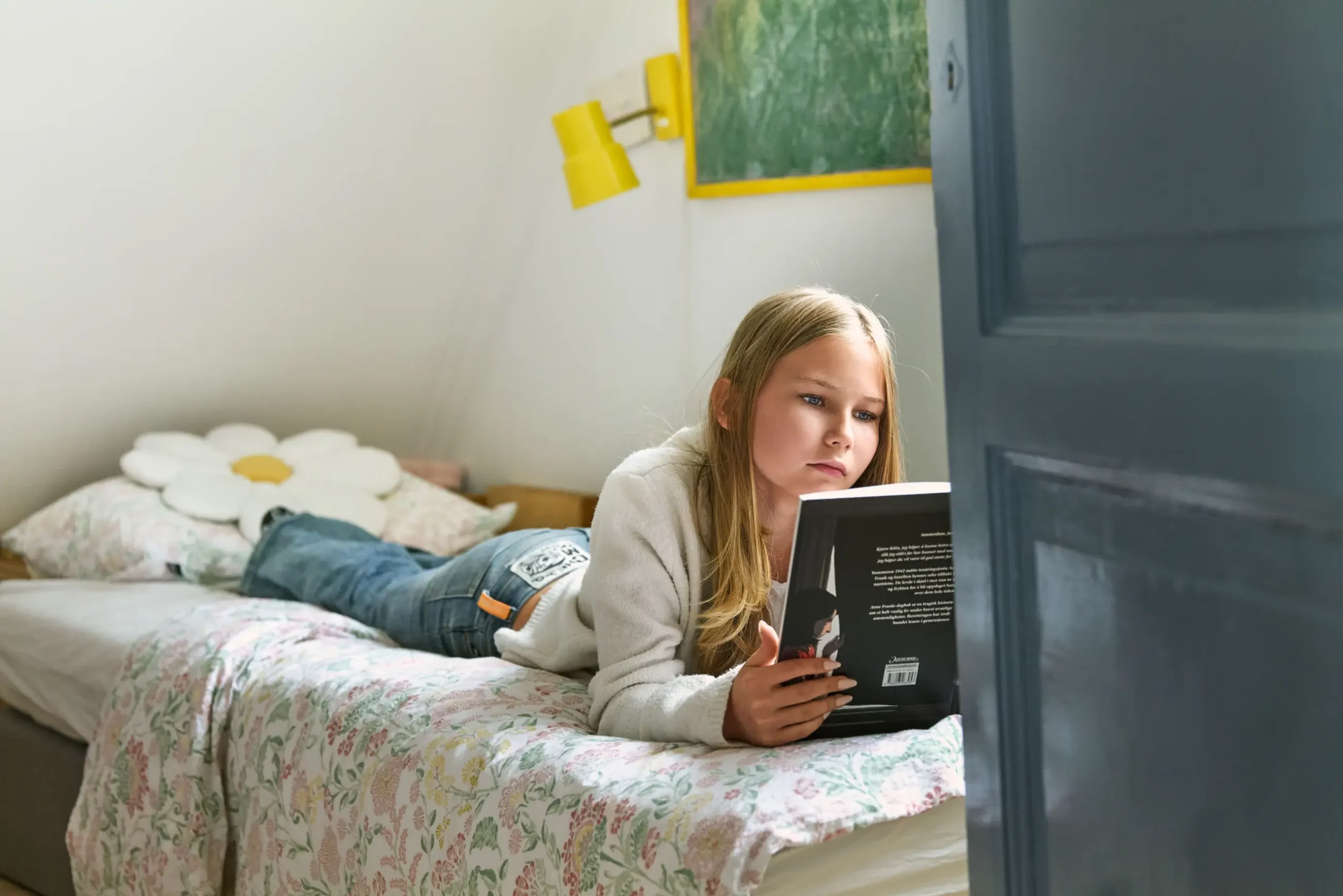 Jente på omtrent 12 år ligger på senga og leser en bok.