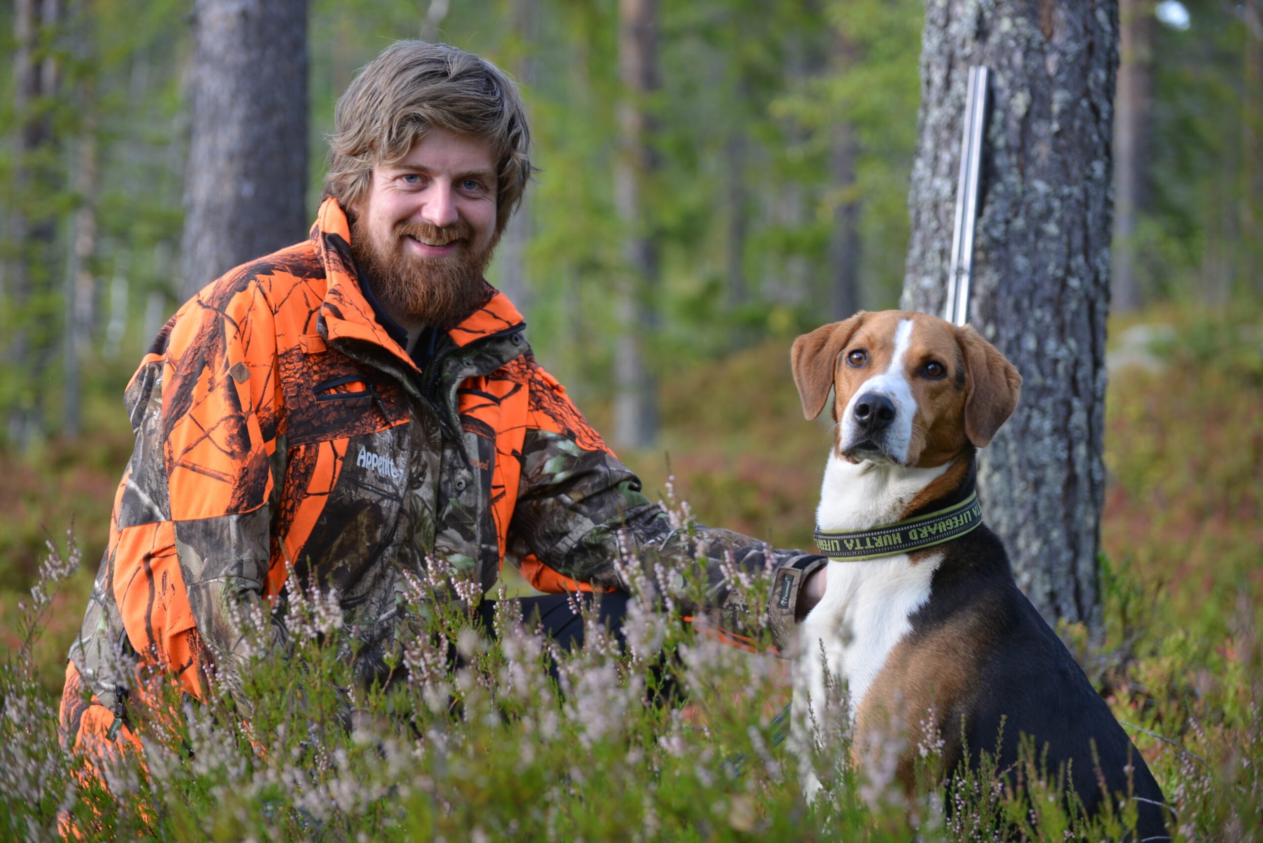 Eivind Lurås, en jeger, er i skogen sammen med hunden sin. Begge smiler og ser i kamera.