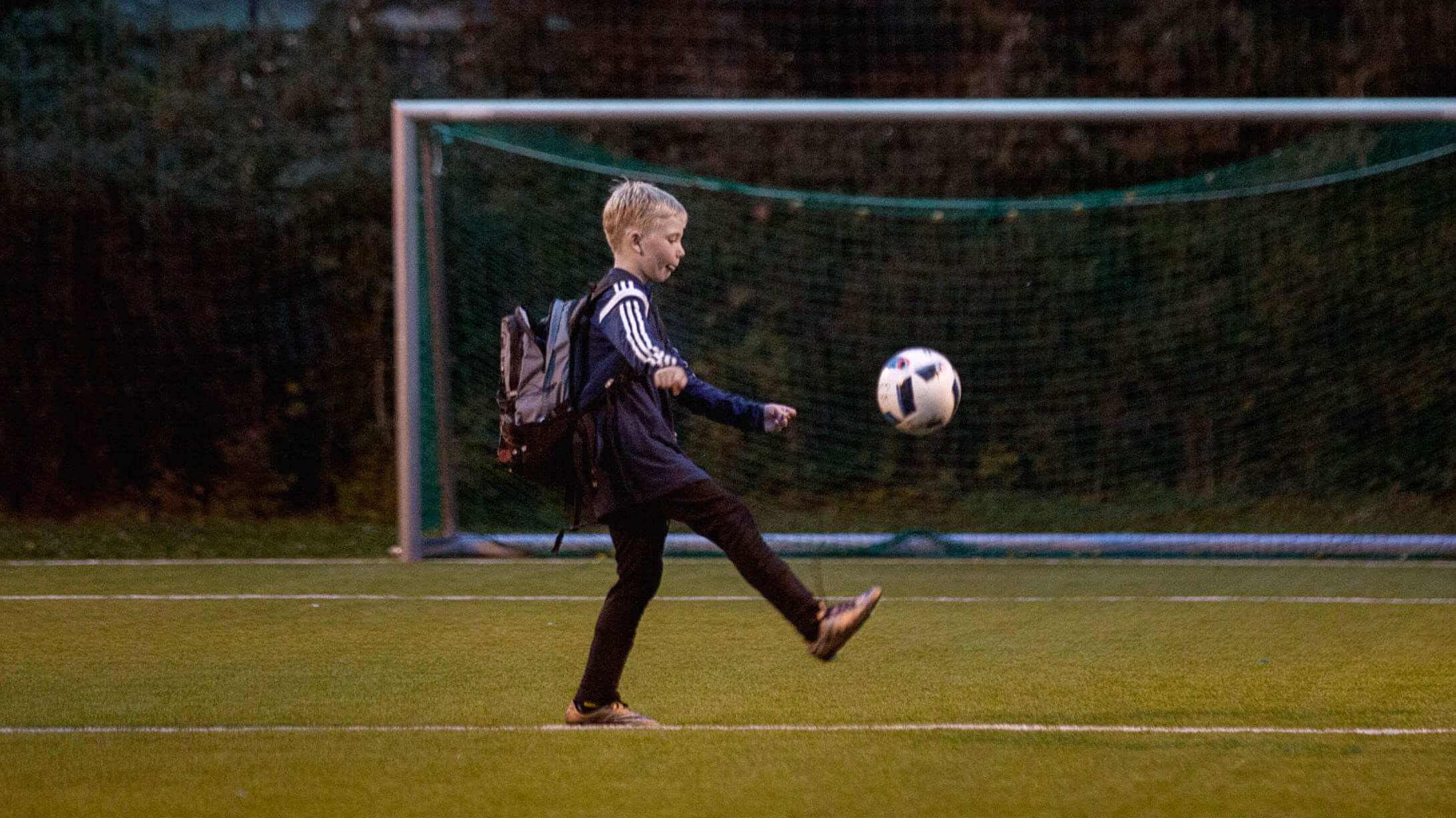 Bilde av en gutt som sparker fotball foran mål