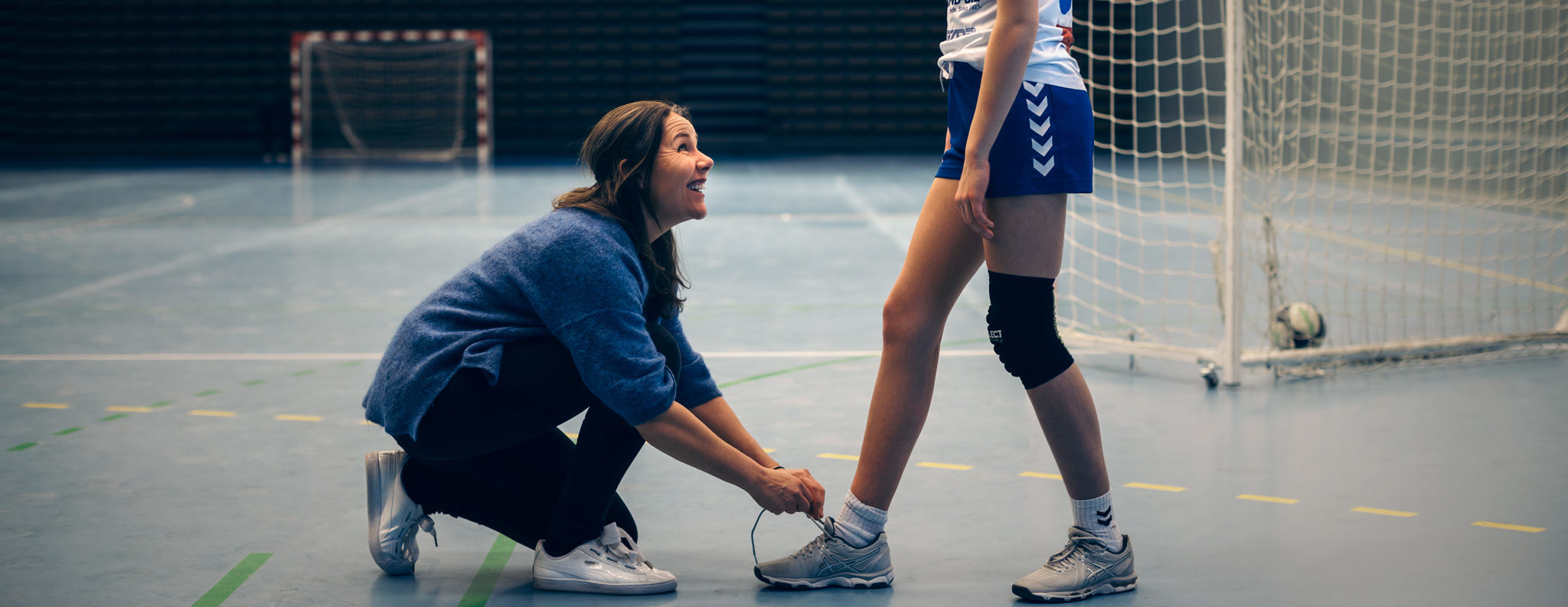 Bilde av trener som knytter lissen på en jente som spiller håndball.