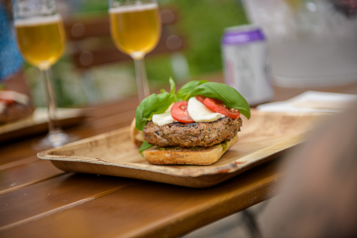 En burger med mozerella, tomat og basilikum. I bakgrunnen kan man se to høye glass fylt med alkoholfri øl, og en boks med Clausthaler pale lager.