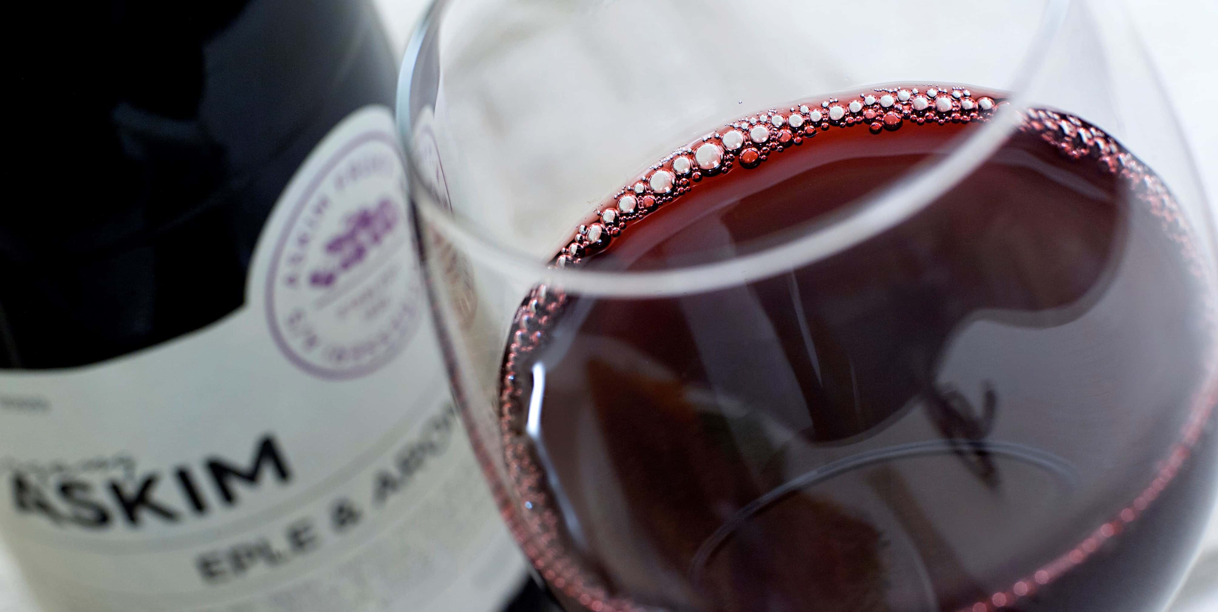 Bilde av Askim Årgang Argonia i vinglass, ved siden av en flaske med samme innhold. Drikken er lilla, og minner om rødvin på farge. Lagt pent frem på en grå duk.