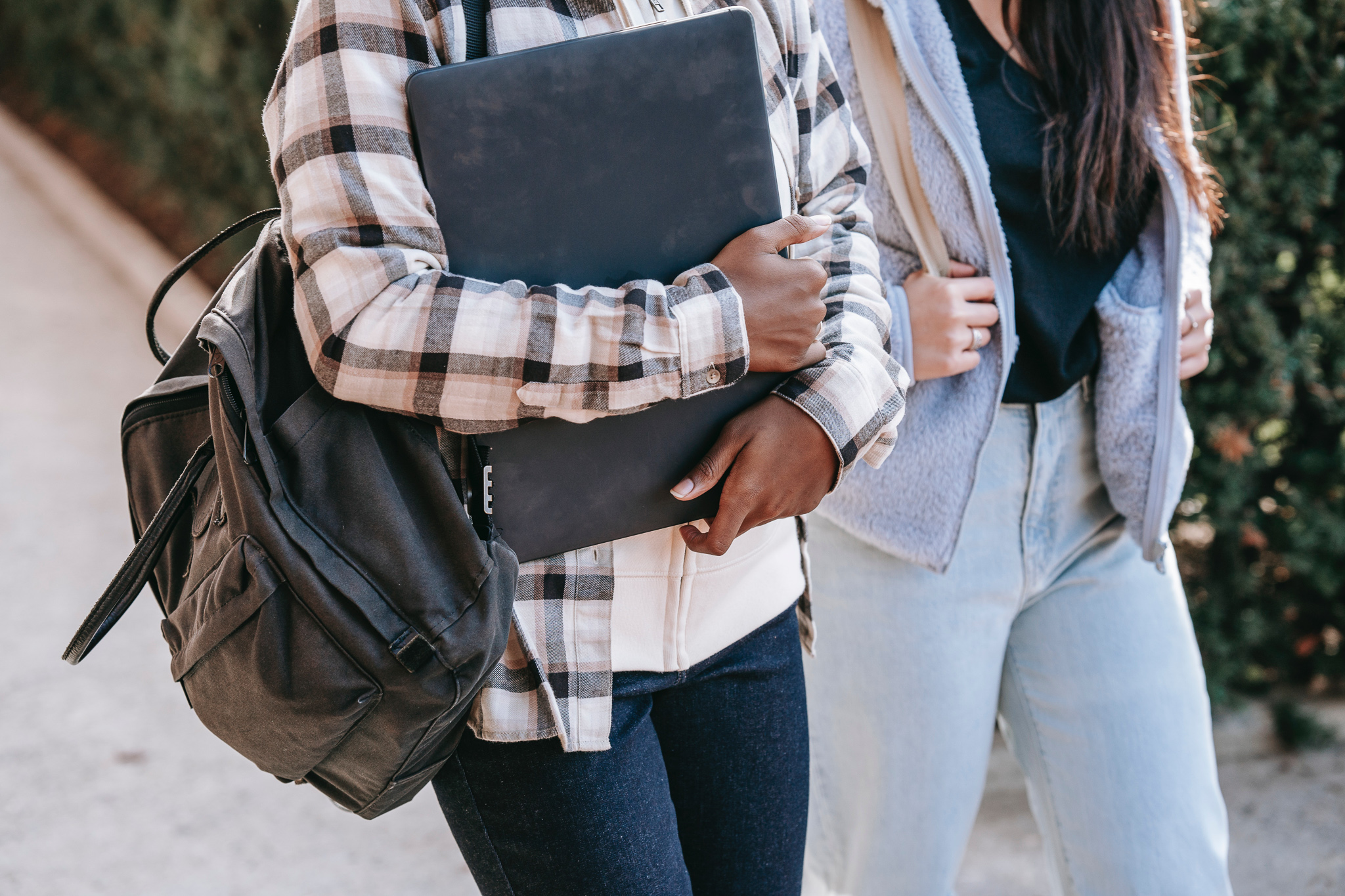 Nærbilde av to jenter som går med skolesekk. Hodene er ikke med på bildet, hun ene bærer en bærbar-pc.