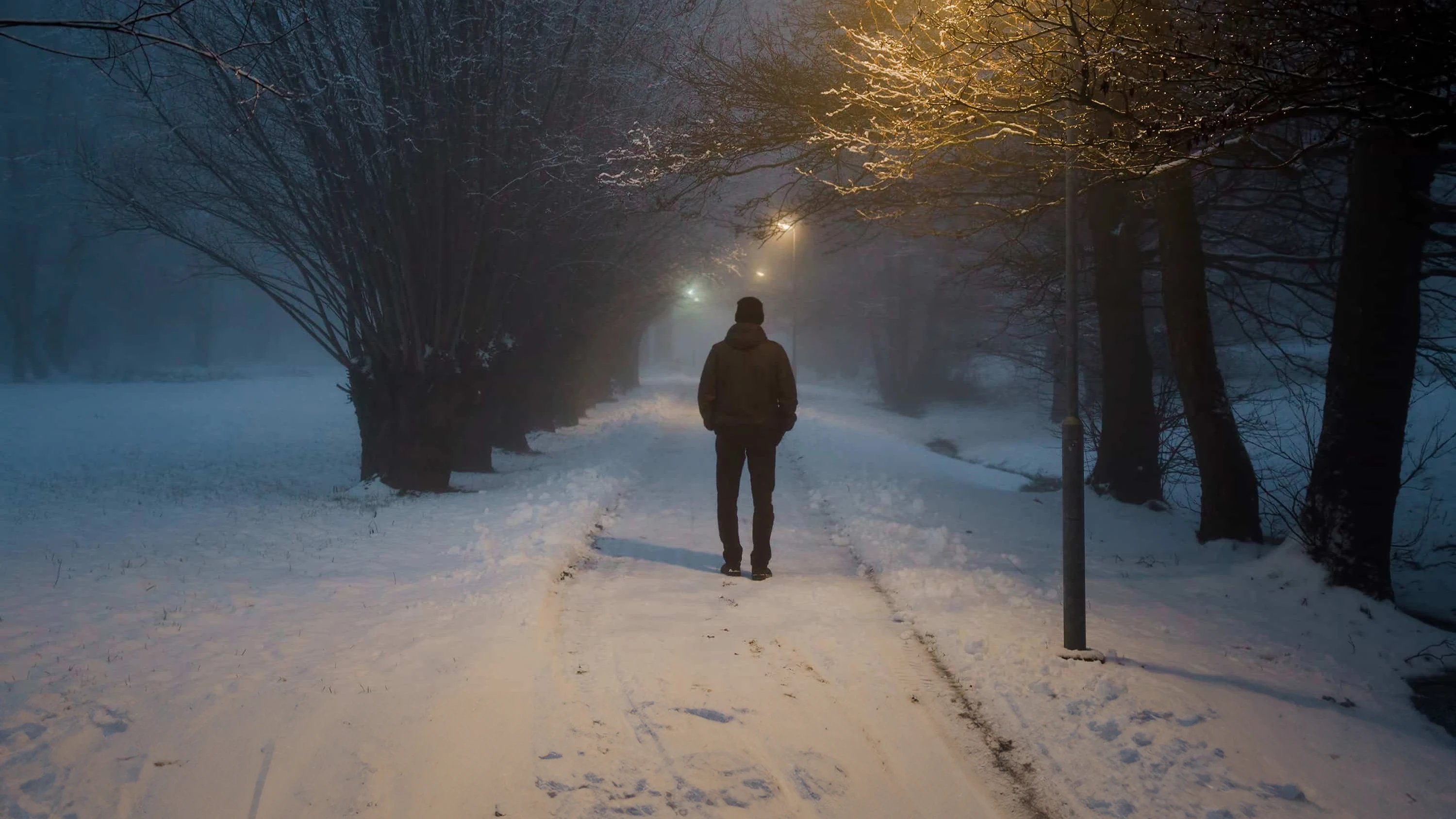 En sortkledd person på en gangvei går i snøen. det ser kaldt ut.