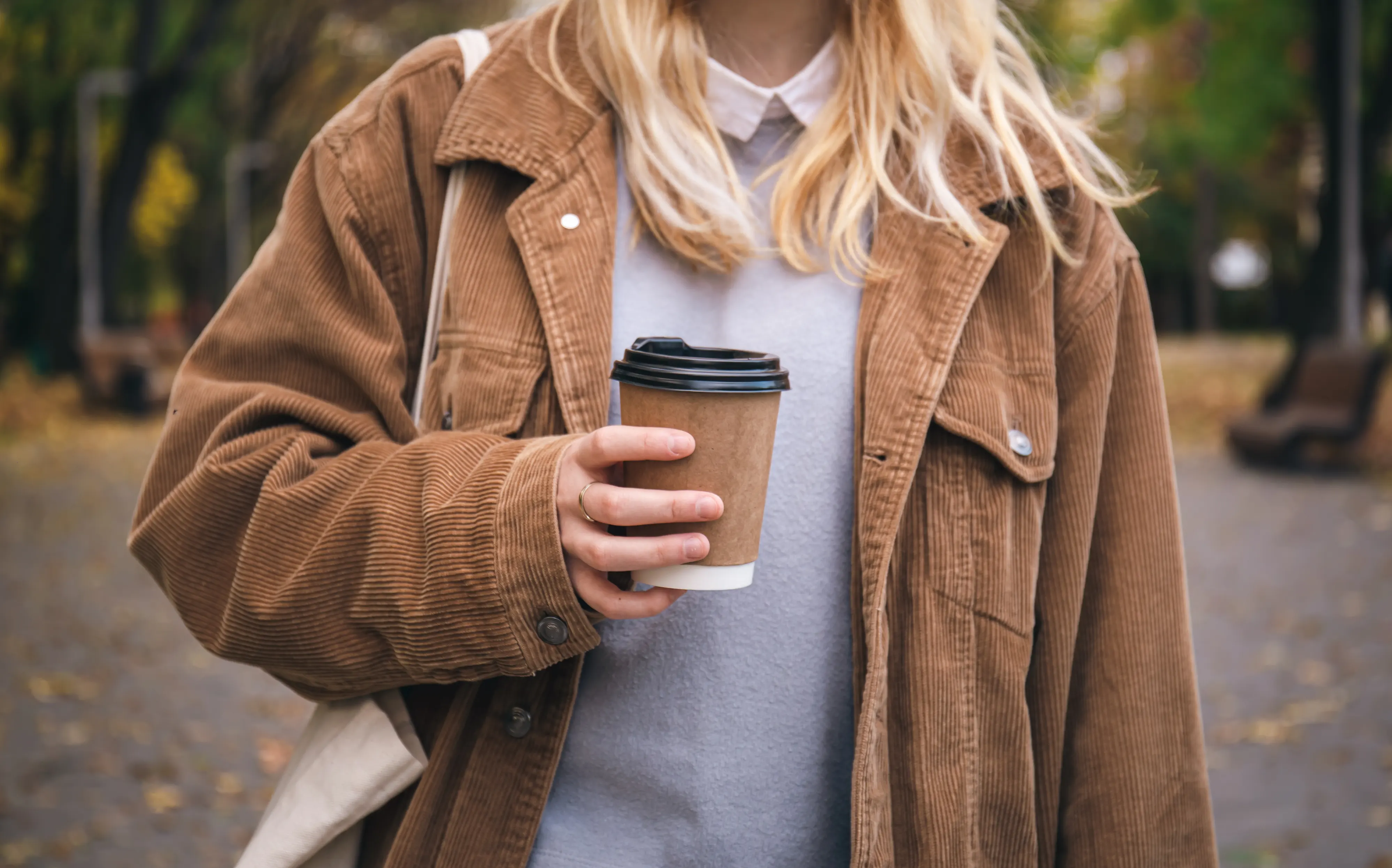 En ung kvinne holder en kopp kaffe i hånden på en tur i parken.