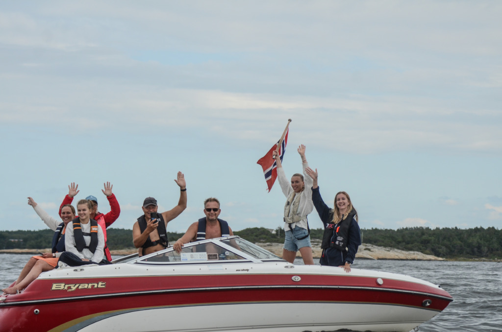 Tilskuere i båt som heier med norgesflagg.