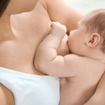 Et spebarn som ligger ved brystet til sin mor og ammer.