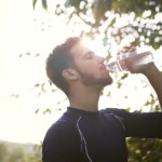 Ung mann som drikker vann fra en flaske i fint vær.