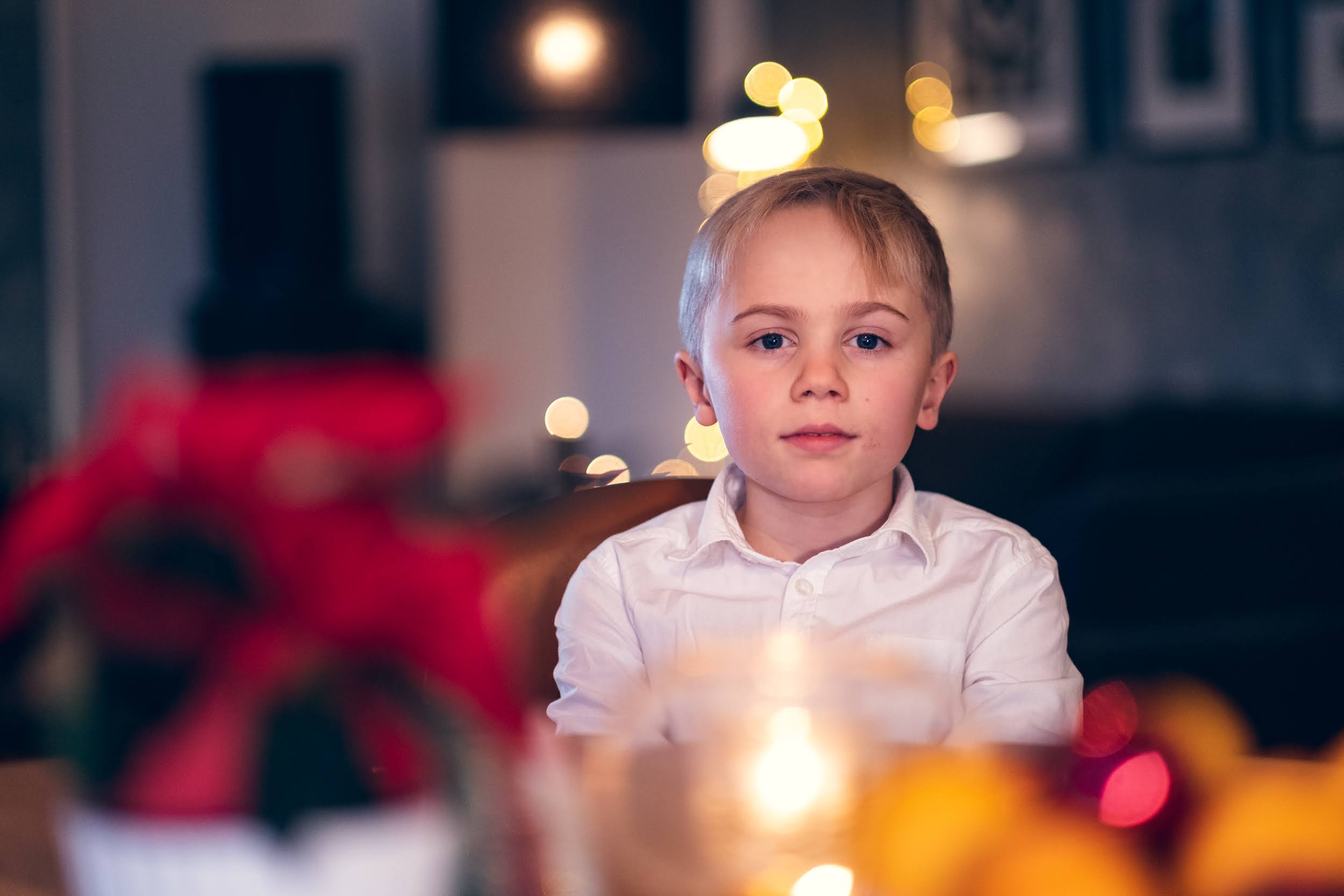 En gutt i hvit skjorte ser inn i kamera. Han sitter i en julepyntet stue.
